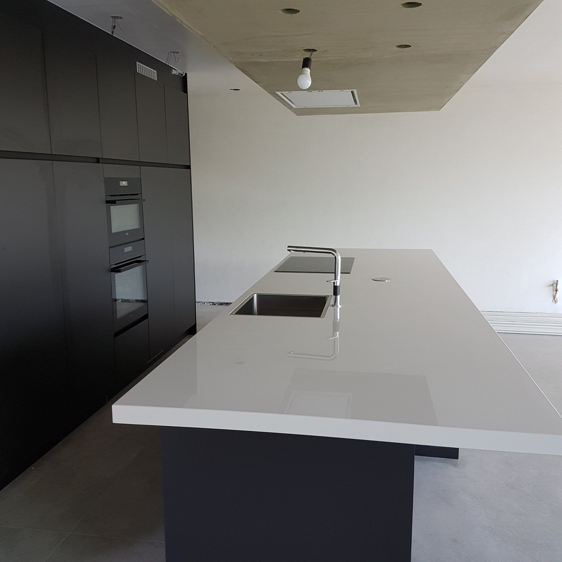 Moderne keuken met een lang wit kookeiland en donkergrijze kasten. De ruimte lijkt in aanbouw.