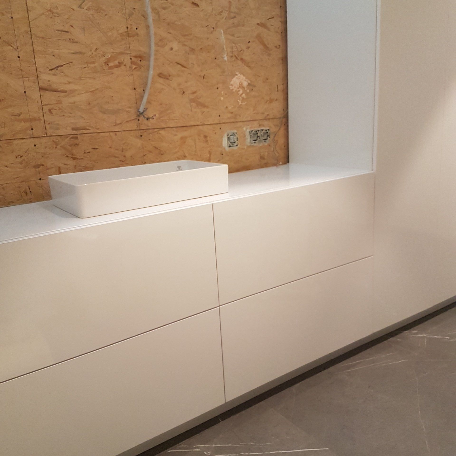 Witte ingebouwde kasten met een aanrechtblad en rechthoekige spoelbak tegen een houten lambrisering; bouw in uitvoering.