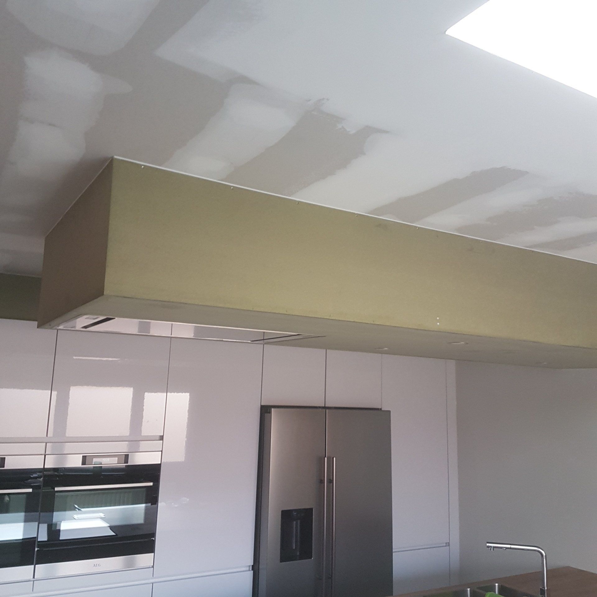 Keuken met witte kasten en een roestvrijstalen koelkast, onder een rechthoekige beige onderkant aan het plafond.