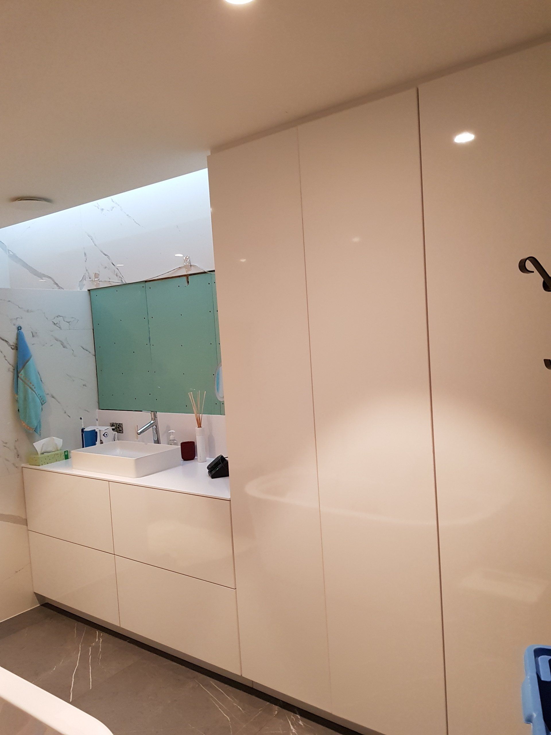 Moderne witte badkamer met grote kasten, wastafel en een aan de muur bevestigde spiegel boven een lang aanrecht.