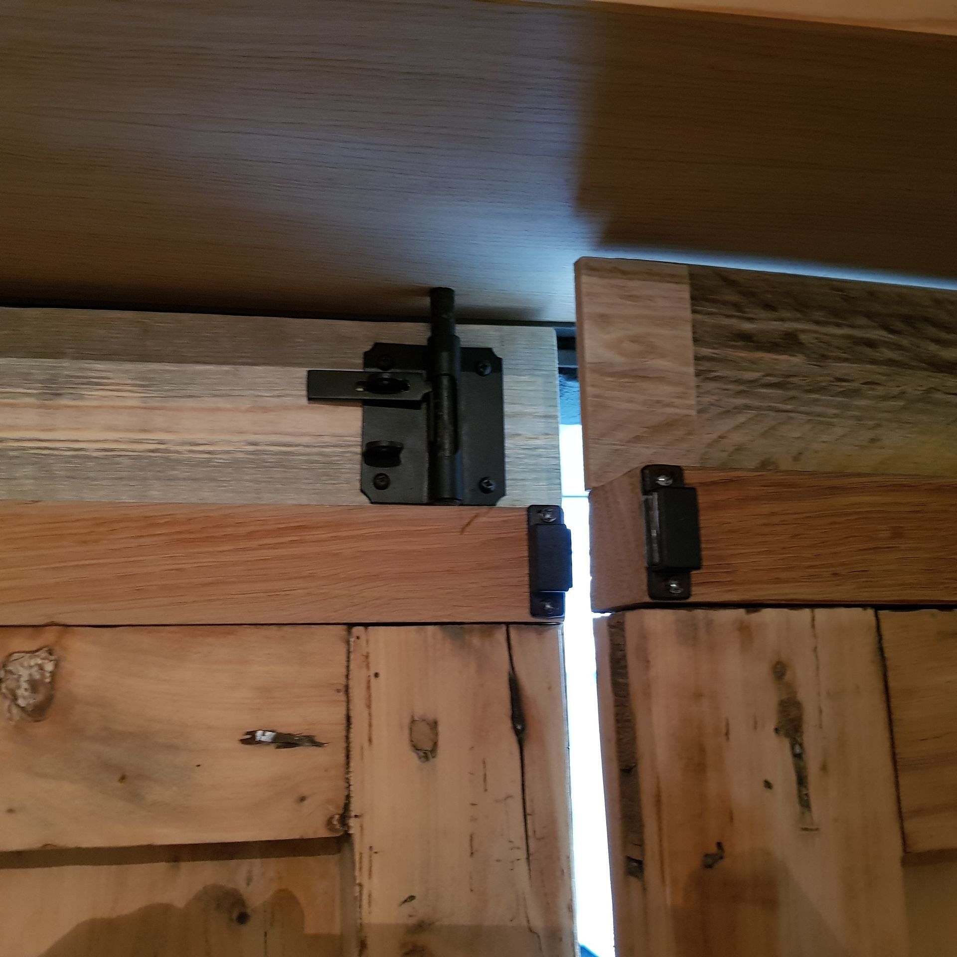 Een close-up van een zwart schuifgrendelslot dat twee houten deuren sluit. De deuren zijn gemaakt van licht en middelkleurig hout.