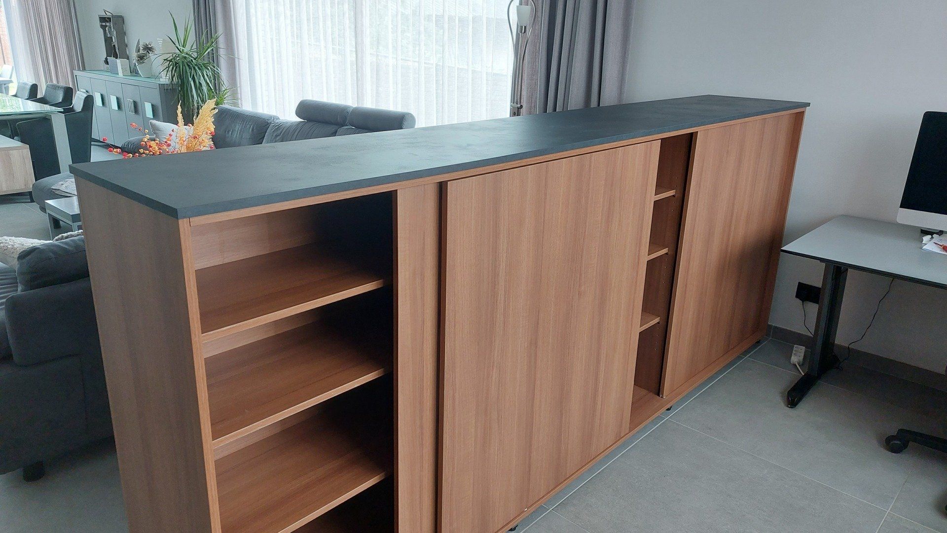 Houten opbergkast met schuifdeuren en open planken tegen een raam, binnenshuis.