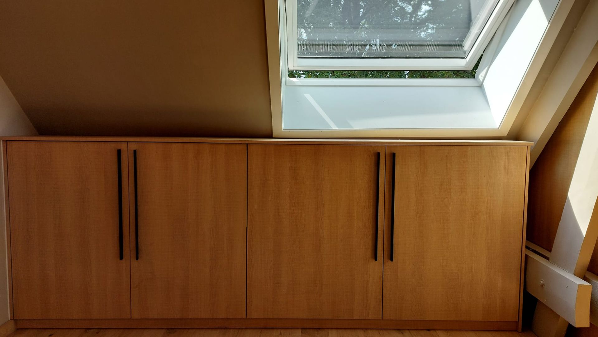 Houten kasten met zwarte handgrepen onder een dakraam in een kamer met houten vloer.