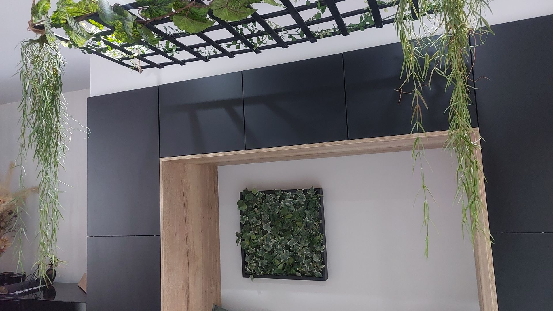 Een moderne binnenruimte met een houten constructie en een groene wand met een plantenrooster en hangend groen.