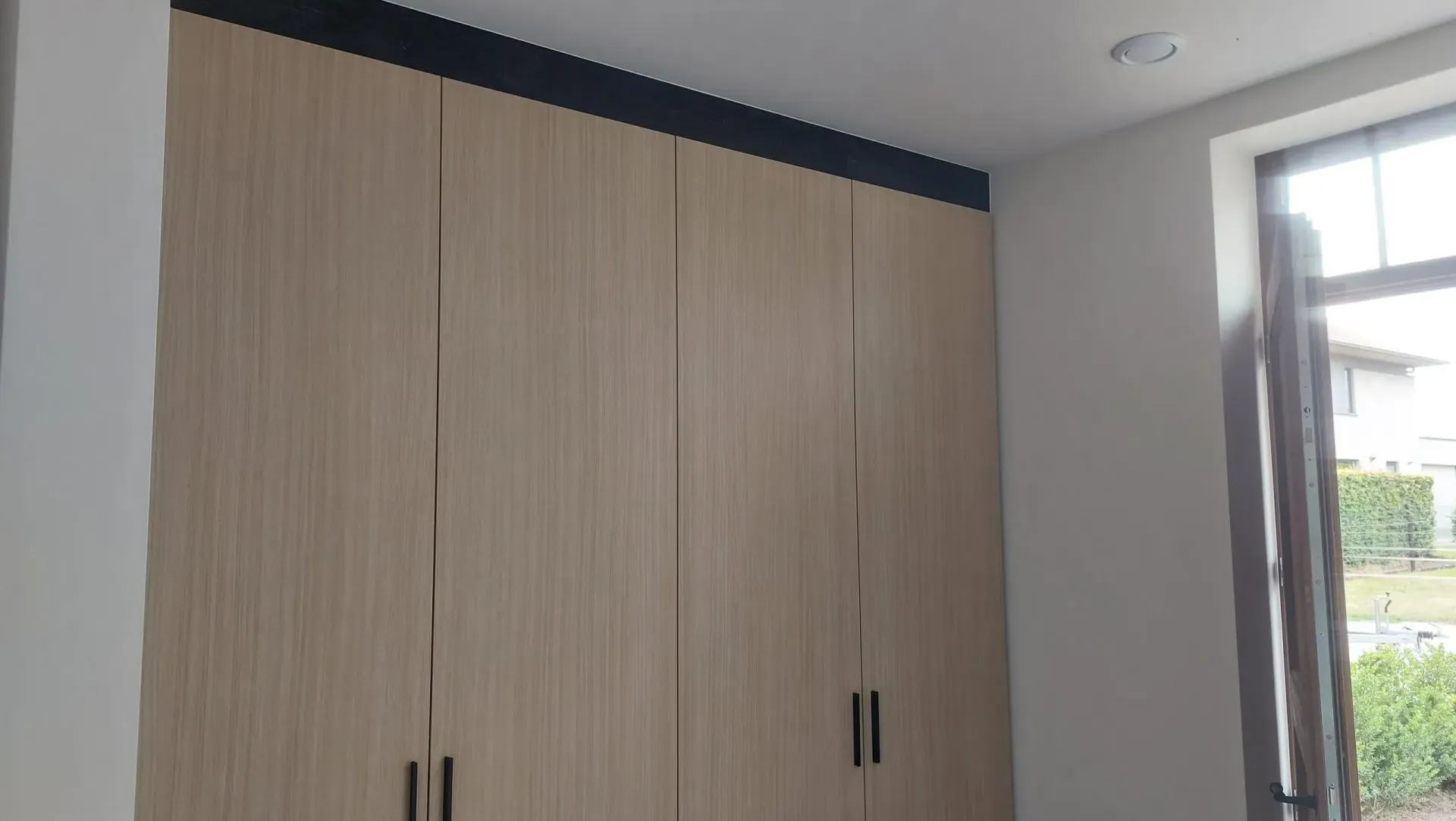 Kast met deuren met lichte houtnerf, zwarte hardware en afwerking. Raam aan de rechterkant.