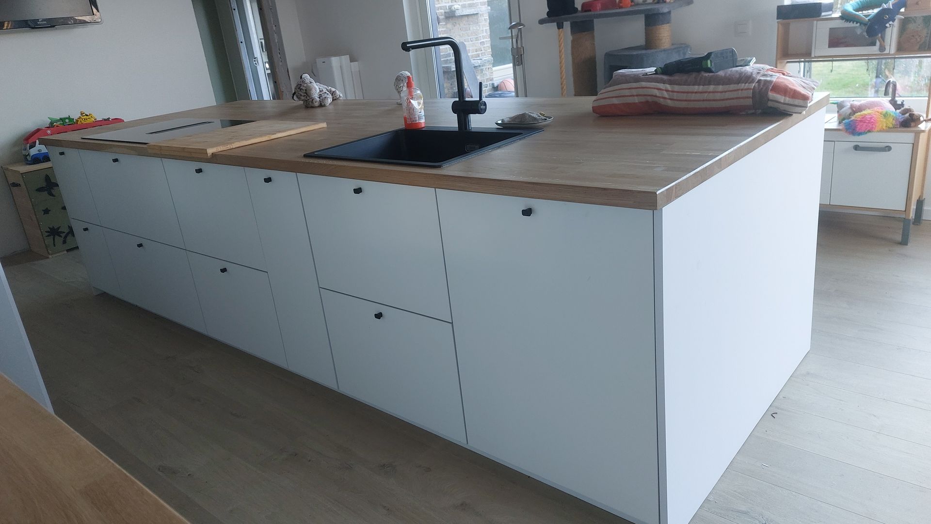 Wit keukeneiland met een houten aanrechtblad, een zwarte spoelbak en witte kastjes met zwarte handgrepen.