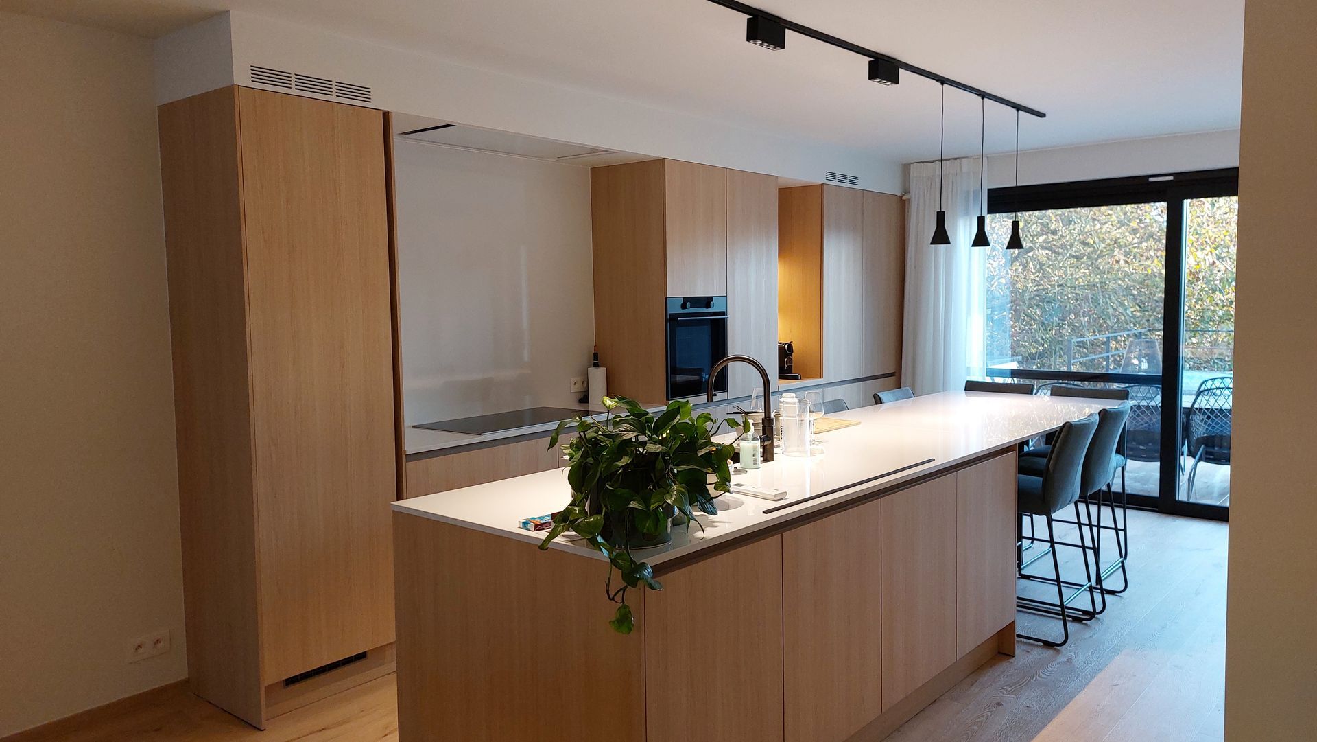 Moderne keuken met lichte houten kasten, een groot kookeiland en een glazen schuifdeur naar het terras.