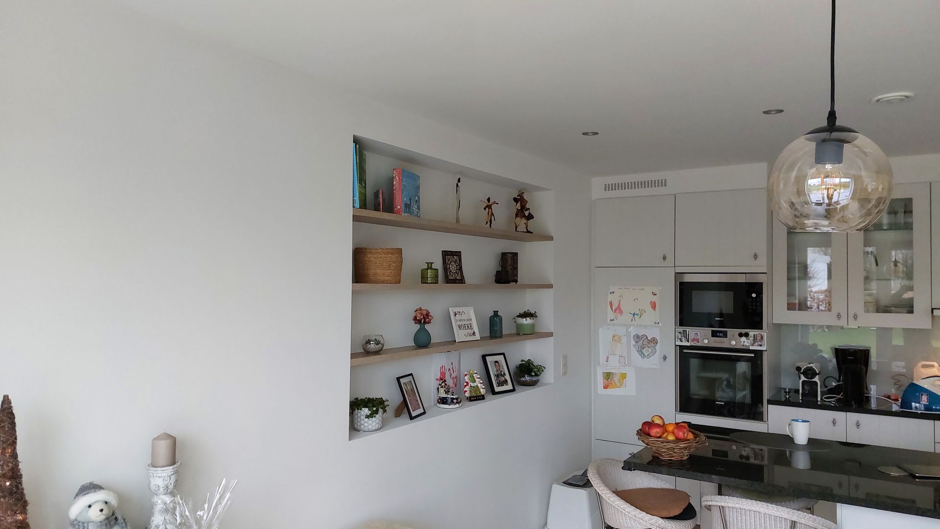 Moderne keuken met lichtgrijze kasten, een donker kookeiland en ingebouwde planken met decoratieve spullen.