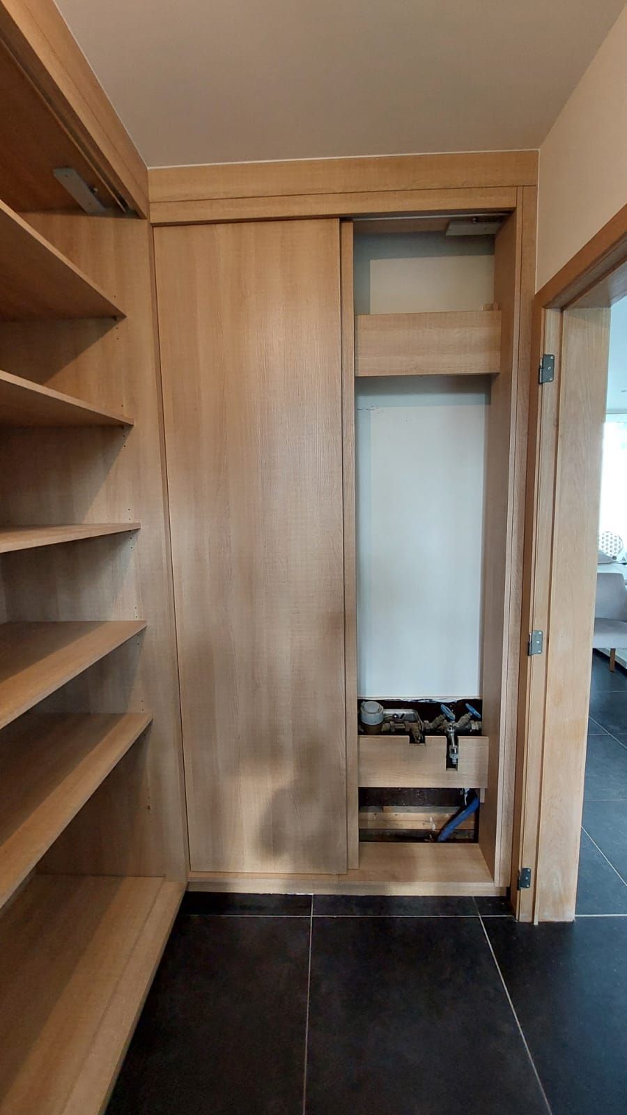 Een houten kast met ingebouwde planken en schuifdeuren. Een deel van de deur is open, waardoor de muur en de opbergruimte zichtbaar zijn.