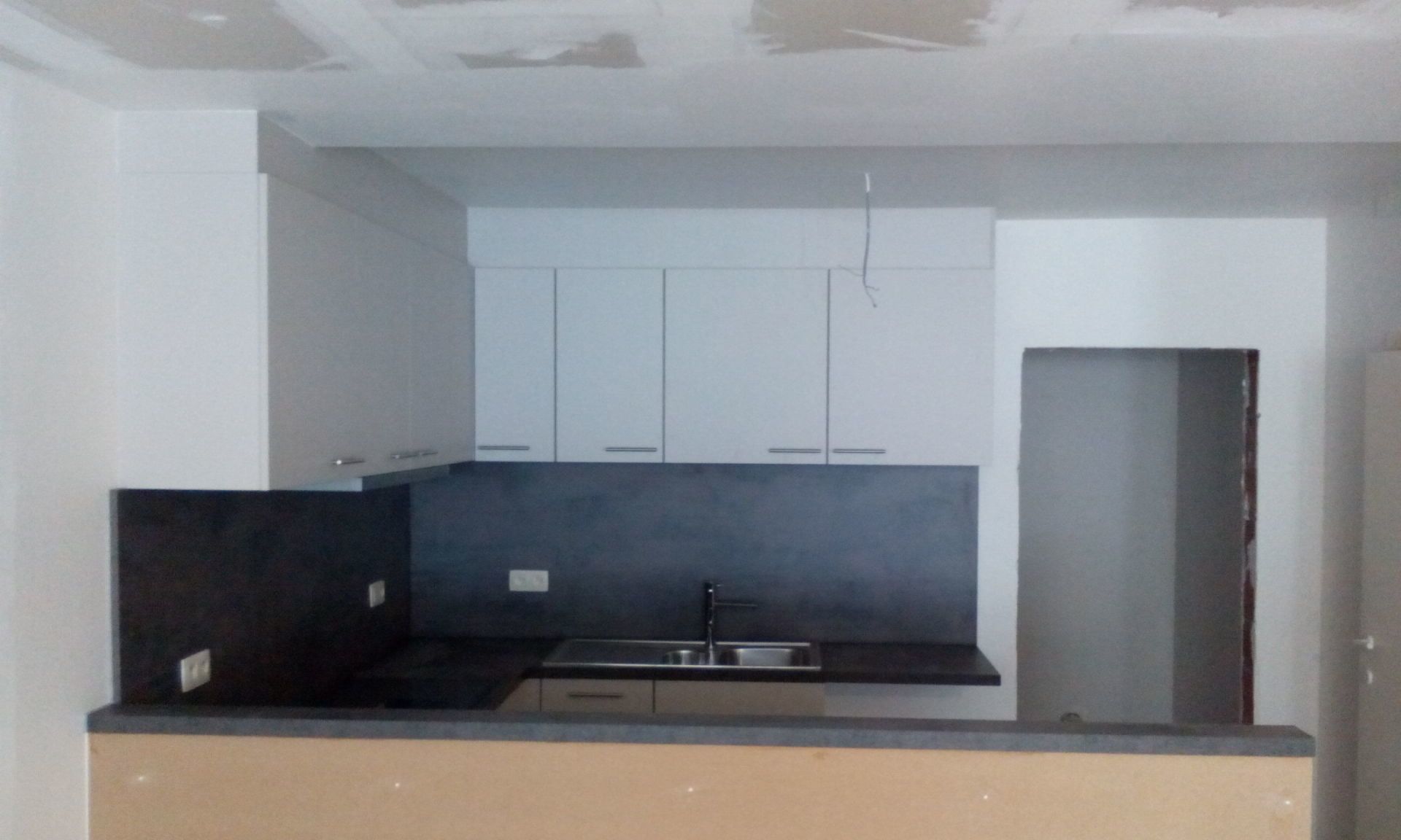 Moderne keuken in aanbouw: witte kasten, grijze achterwand en donker aanrechtblad. Onafgewerkte muren en deuropening.