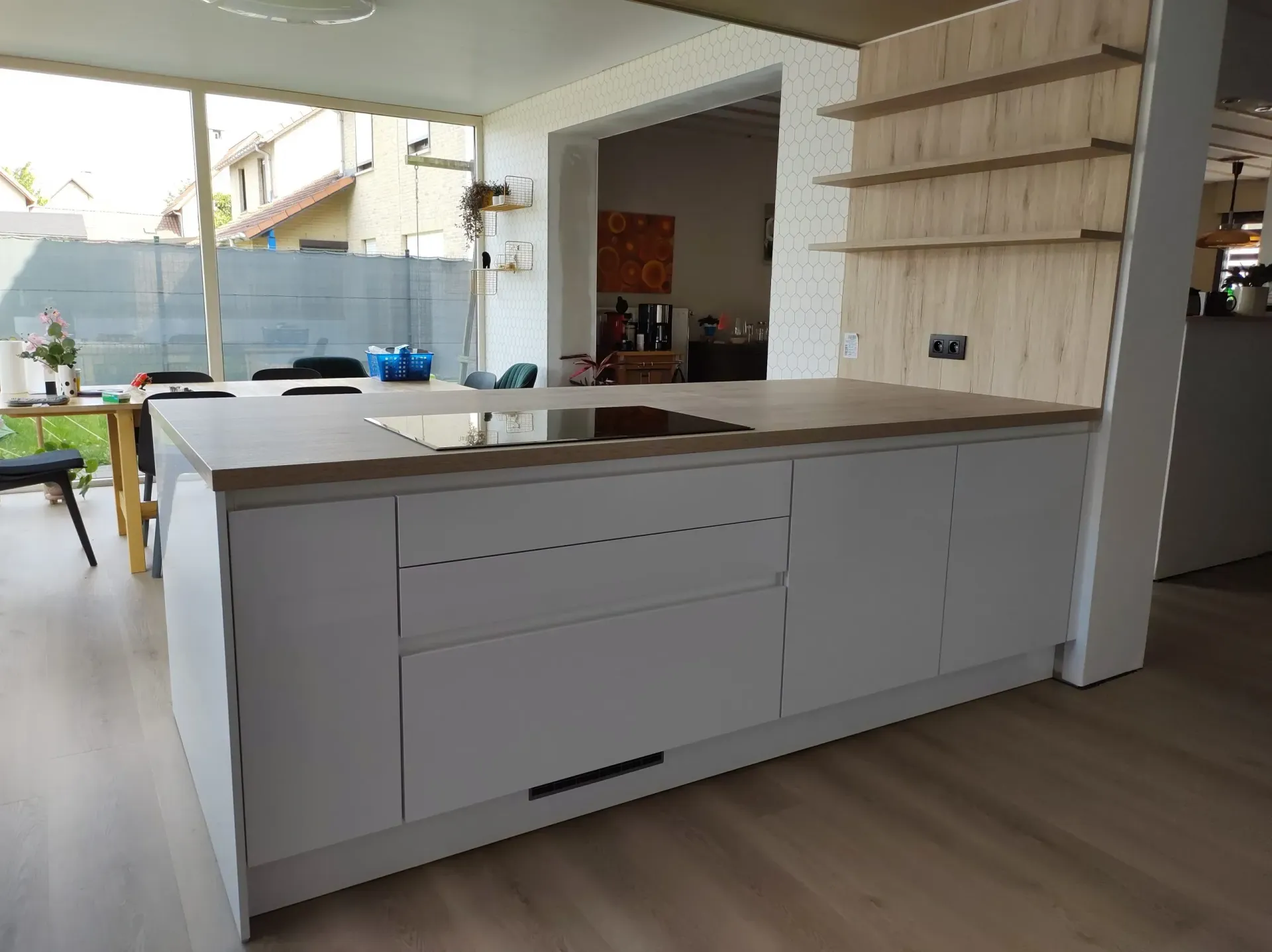 Modern kookeiland met licht houten aanrechtblad en grijze kasten, in een kamer met hardhouten vloeren en een serre.