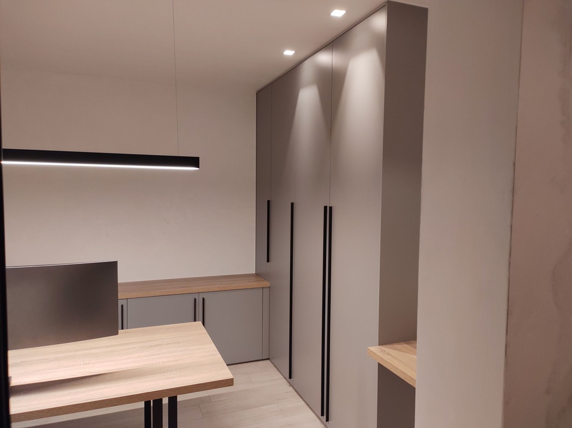 Een moderne kantoorruimte met grijze kasten, houten bureaus en een zwarte lineaire lamp.