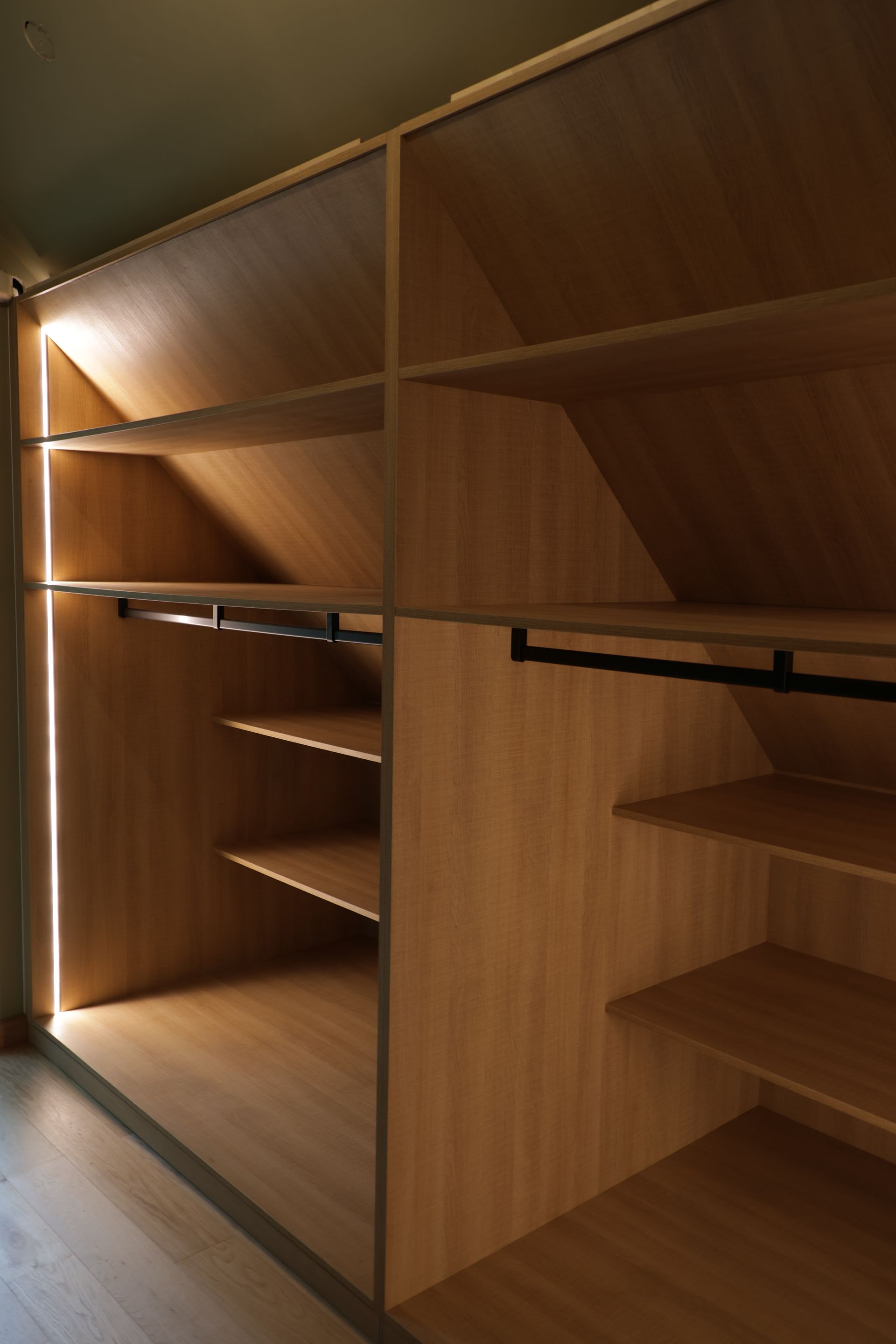 Binnenin een houten kast met planken en hangstangen, verlicht door verborgen verlichting.
