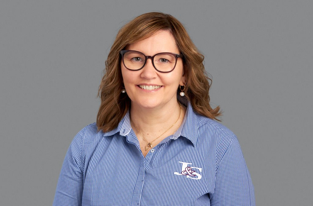 A woman wearing glasses and a blue striped shirt is smiling.