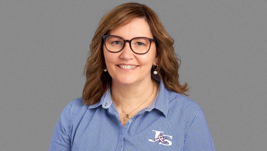 A woman wearing glasses and a blue striped shirt is smiling.