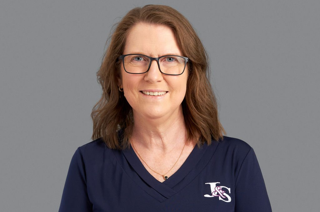 A woman wearing glasses and a blue shirt is smiling for the camera.