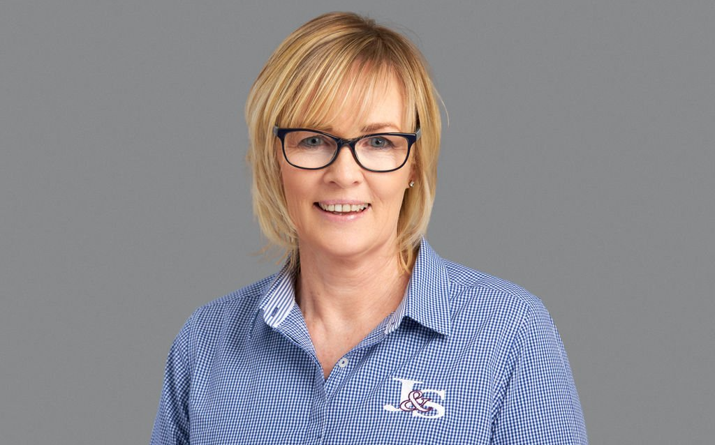 A woman wearing glasses and a blue striped shirt is smiling.