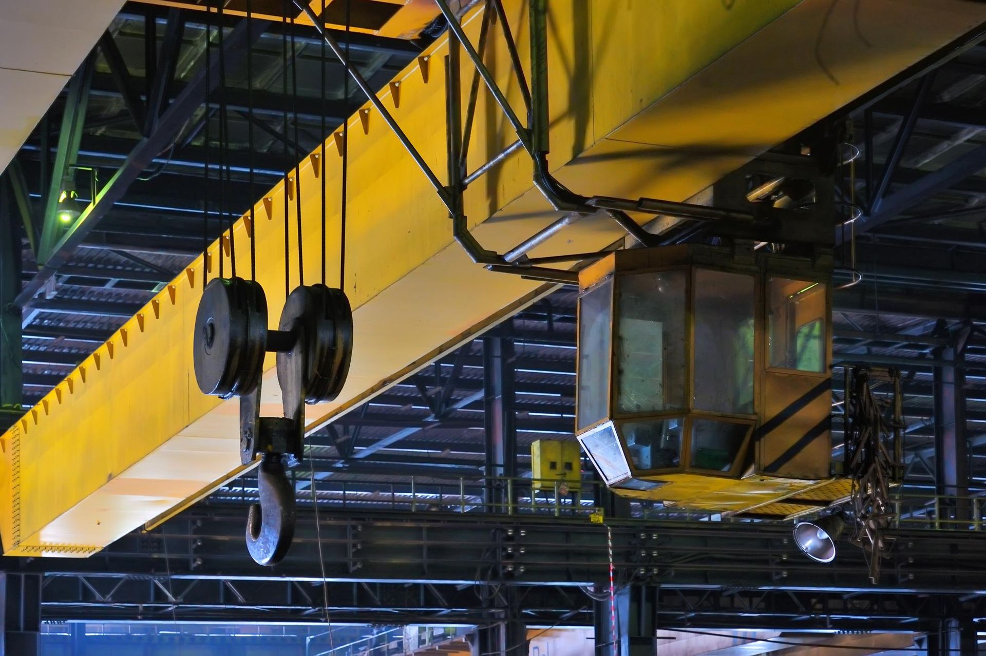 Yellow overhead crane in a factory, with a suspended hook and operator cab.
