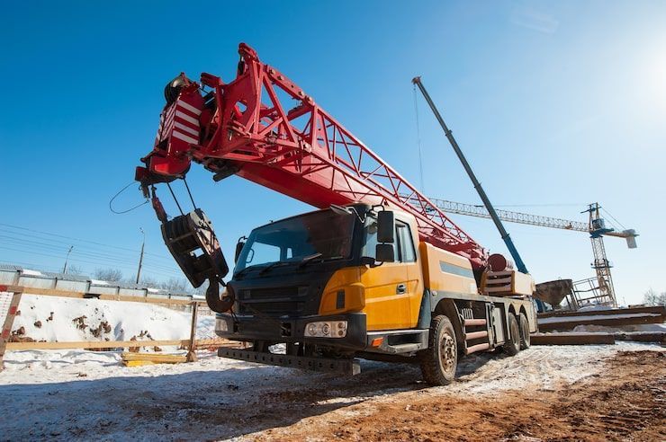 Yellow mobile crane on construction site with red boom against a blue sky.