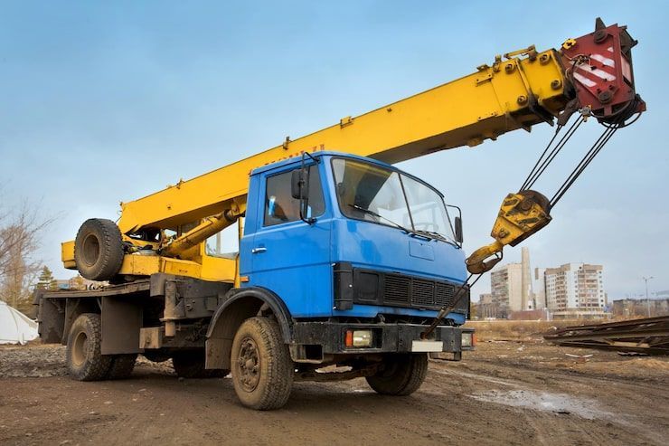 Blue and yellow crane truck on a construction site, raised arm.