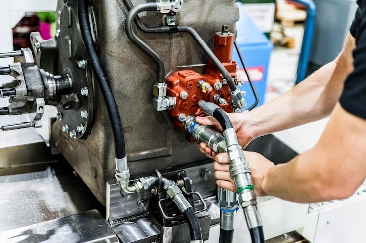 Person connecting hydraulic hoses to a red pump on machinery.