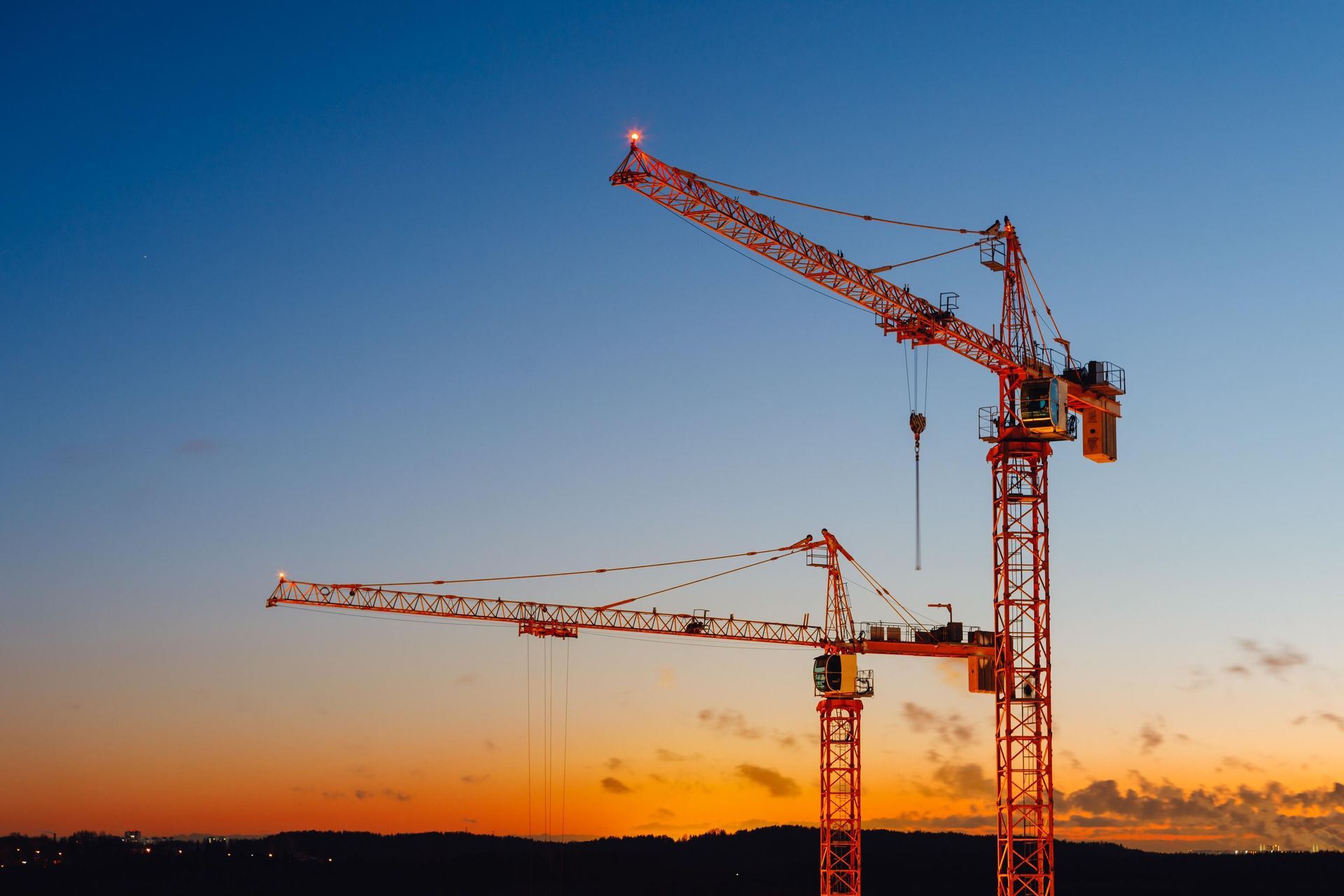 Two orange construction cranes against a dusk sky.