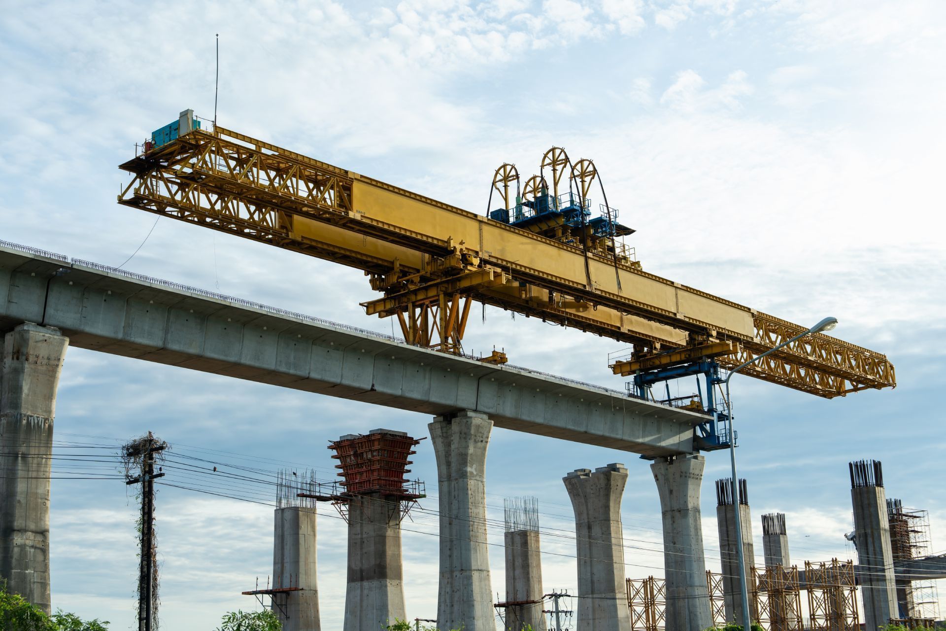 Construction crane placing a concrete beam on supporting pillars; cloudy sky background.