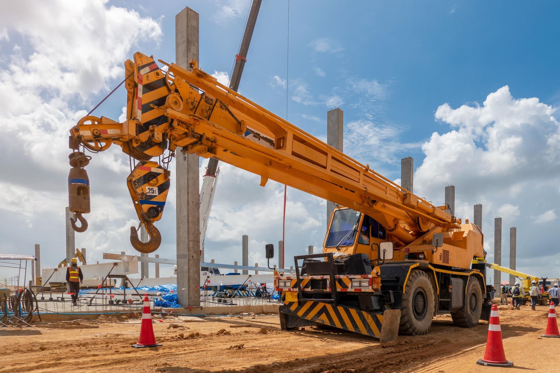 Yellow mobile crane at construction site, lifting equipment. Concrete pillars and blue sky visible.