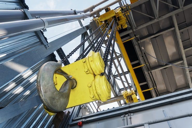 Yellow crane hook and pulley system inside industrial structure.