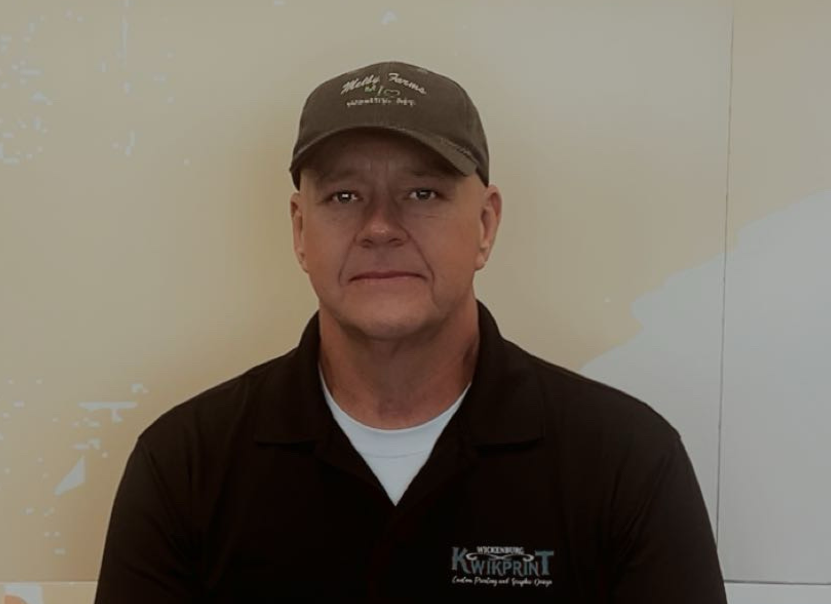 Man in black polo and cap against a beige wall.