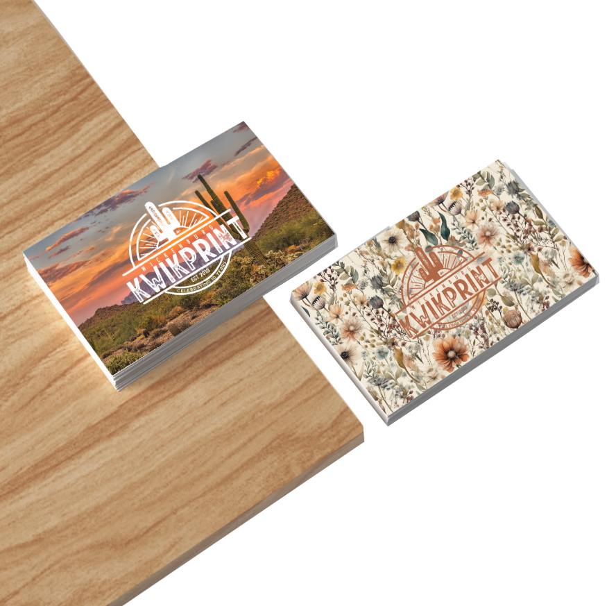 Two stacks of business cards on wood. One shows a desert sunset, the other a floral pattern; both have a logo.