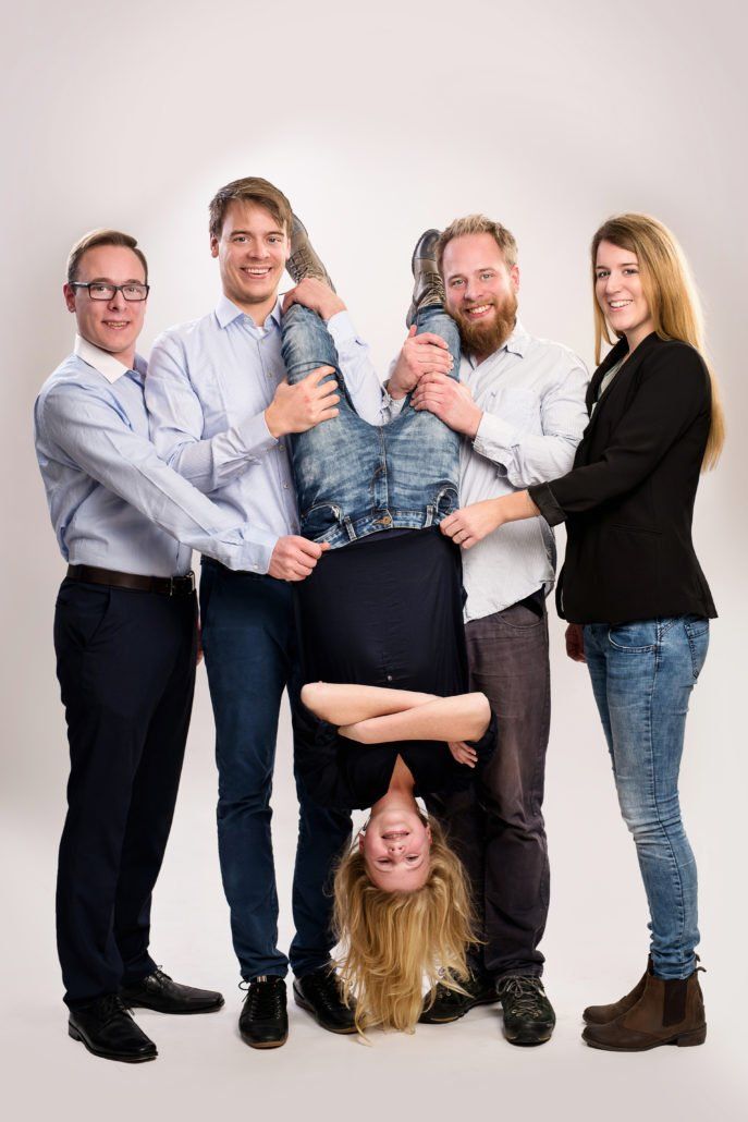 Eine Gruppe von Menschen posiert für ein Foto mit einer kopfüber hängenden Frau.