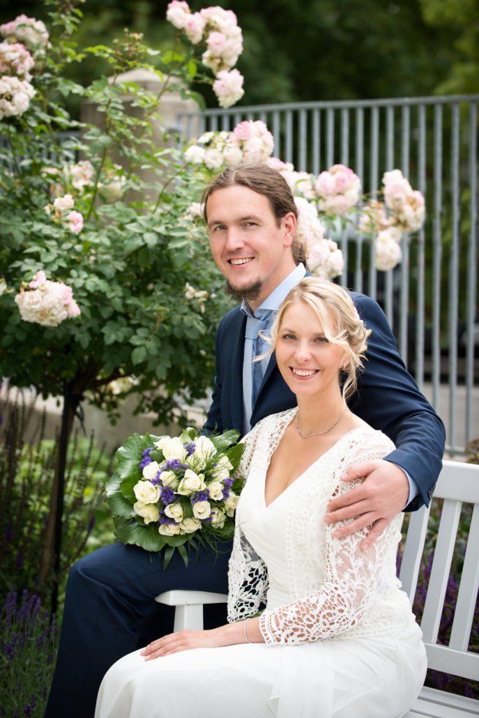 Eine Braut und ein Bräutigam posieren auf einer Bank sitzend für ein Foto.