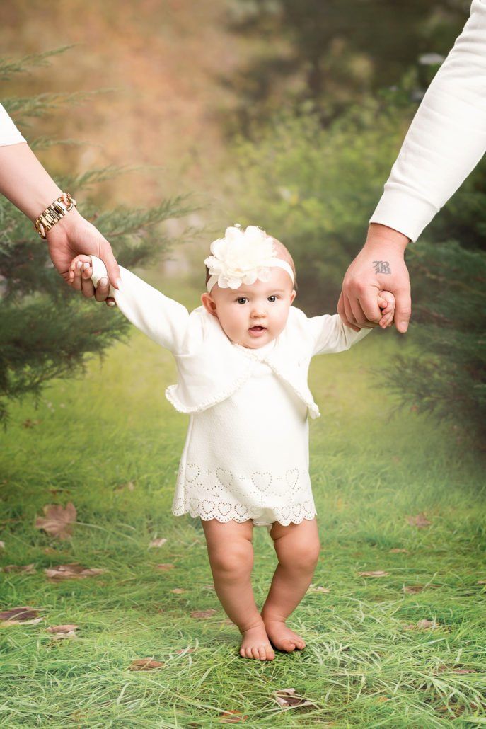 Ein kleines Mädchen in einem weißen Kleid hält die Hände seiner Eltern.