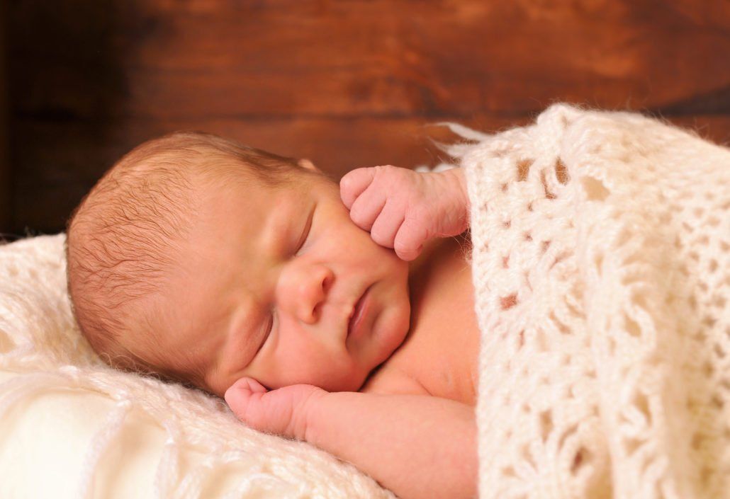 Ein neugeborenes Baby schläft auf einer weißen Decke.