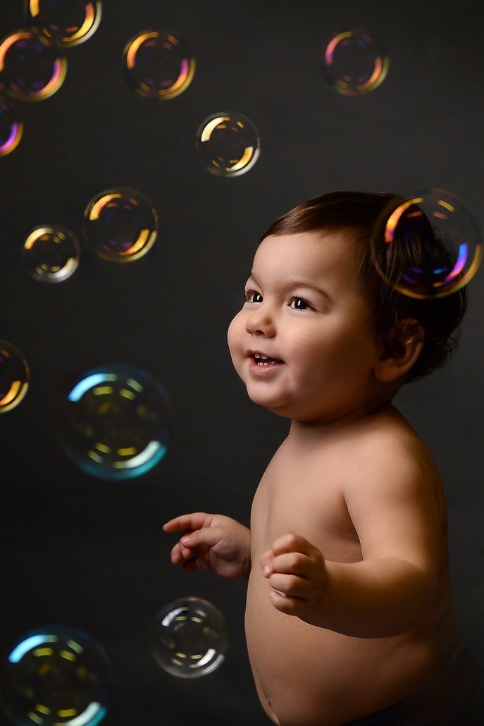 Ein Baby spielt mit Seifenblasen auf einem schwarzen Hintergrund.