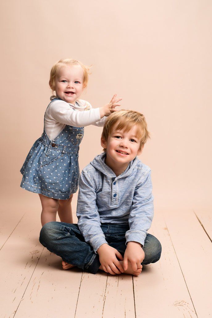 Ein kleines Mädchen steht neben einem kleinen Jungen, der auf dem Boden sitzt.