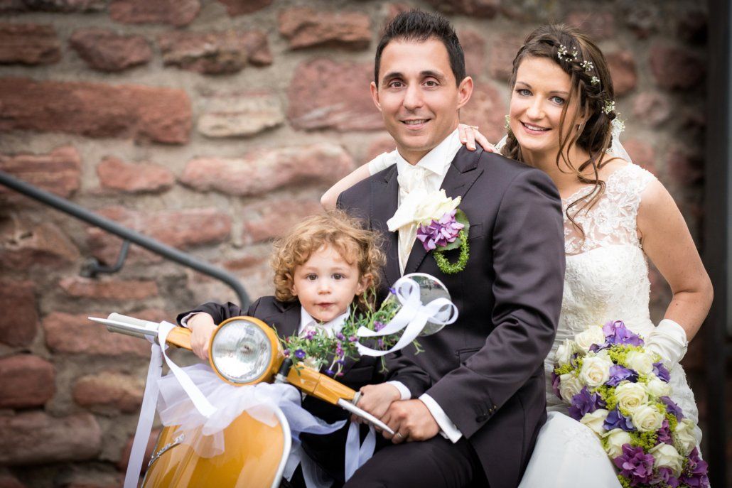 Ein Brautpaar posiert für ein Foto mit einem kleinen Jungen auf einem Roller.