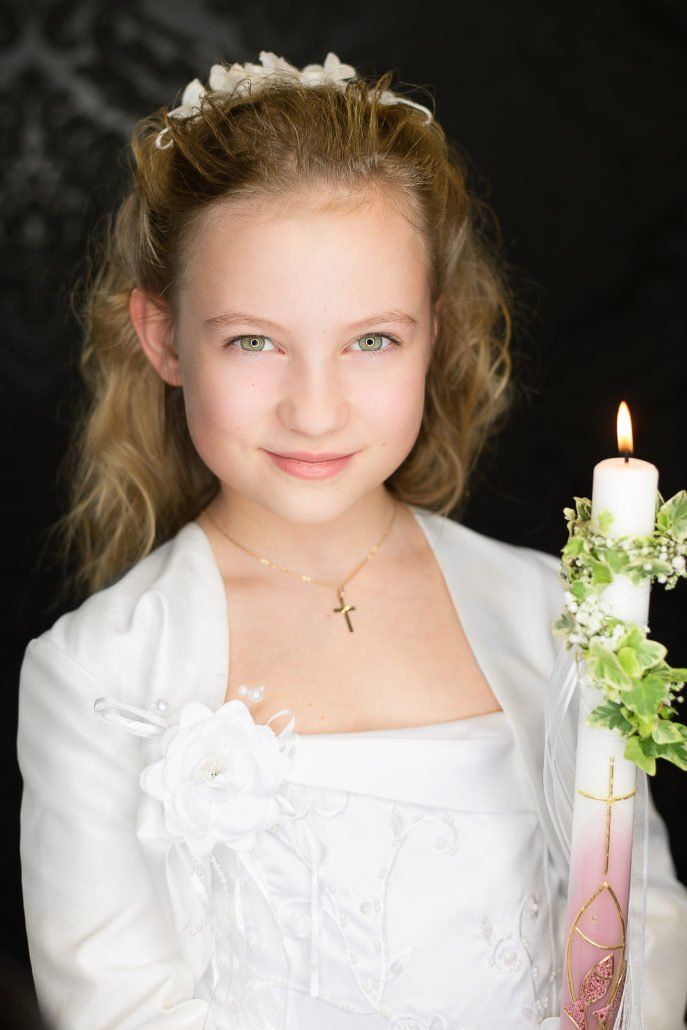 Ein junges Mädchen in einem weißen Kleid hält eine Kerze