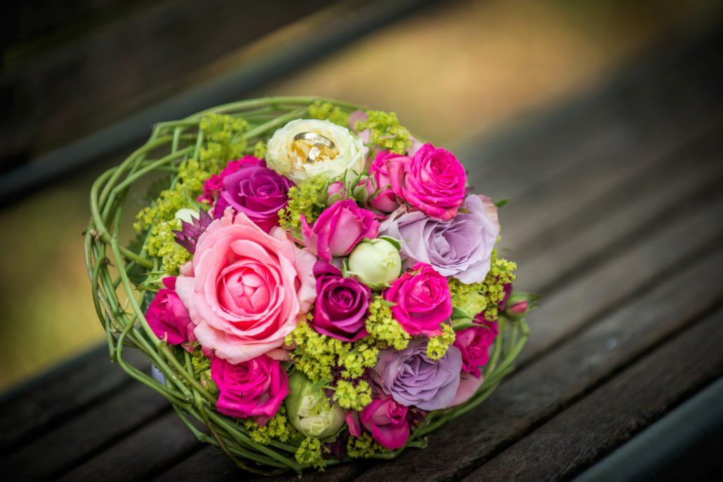 Auf einer Holzbank steht ein Strauß rosa und violetter Blumen.