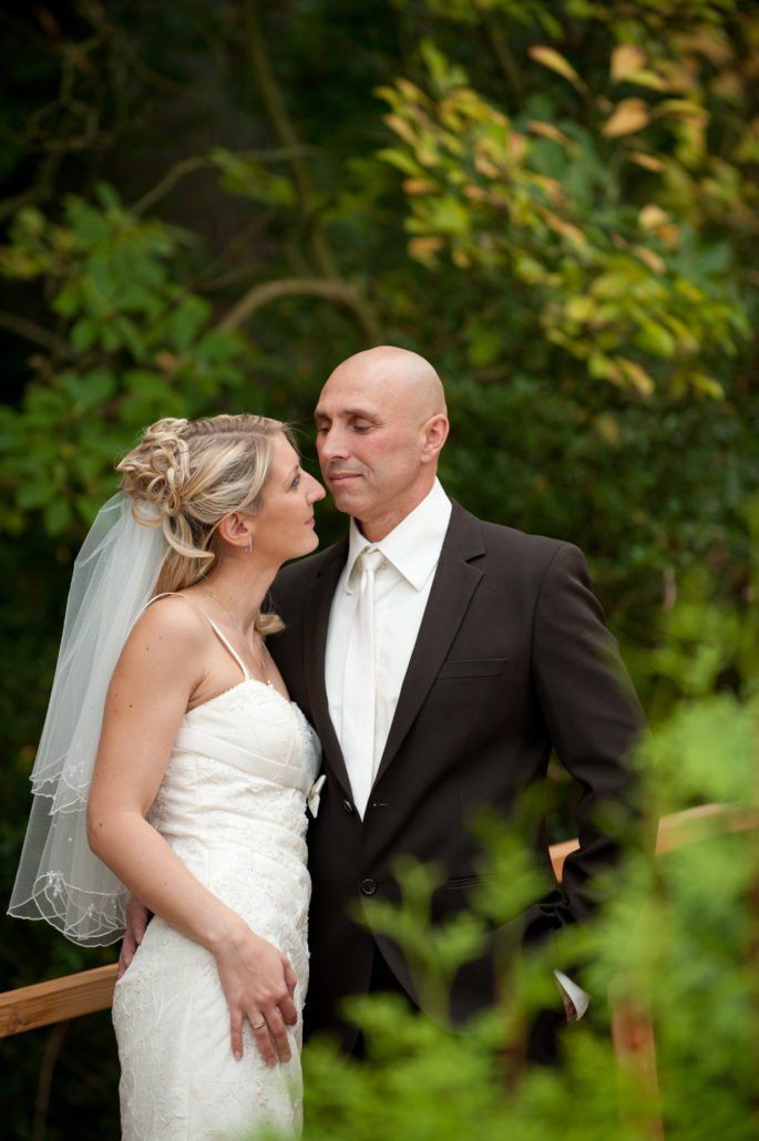 Eine Braut und ein Bräutigam küssen sich auf einer Brücke im Wald.