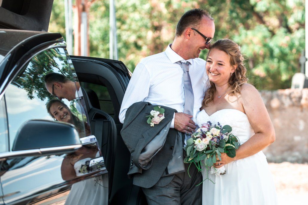 Eine Braut und ein Bräutigam stehen neben einem Auto.