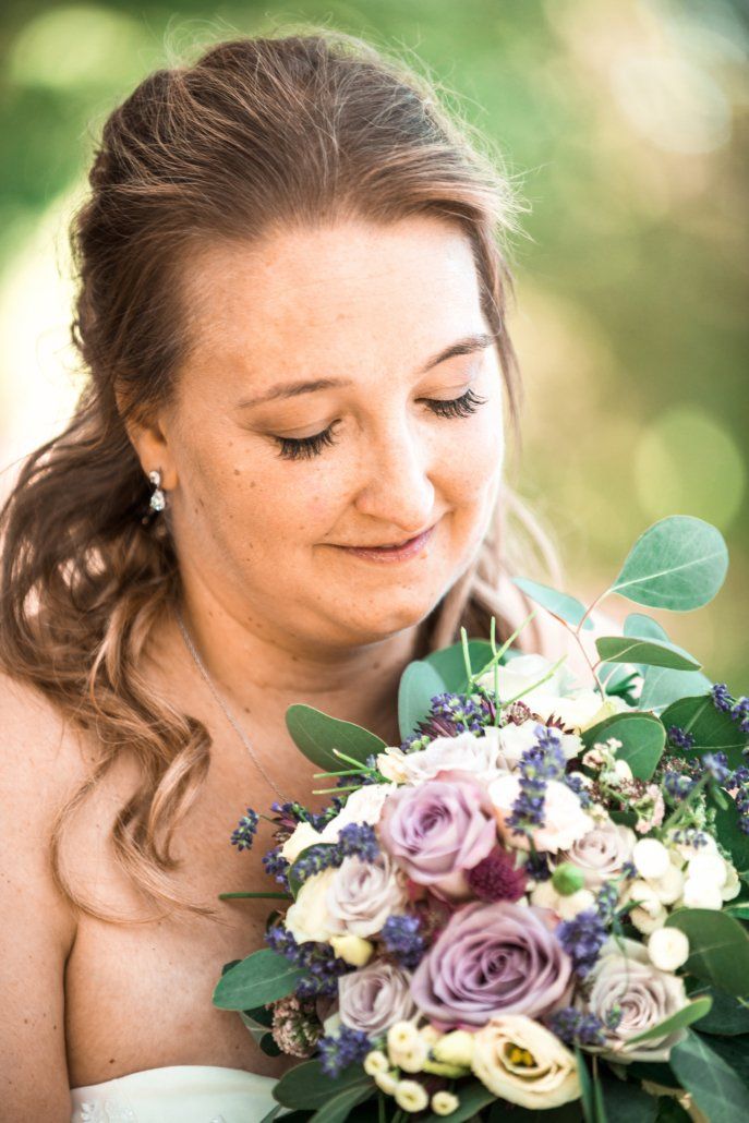 Eine Braut hält einen Strauß violetter und weißer Blumen in der Hand.