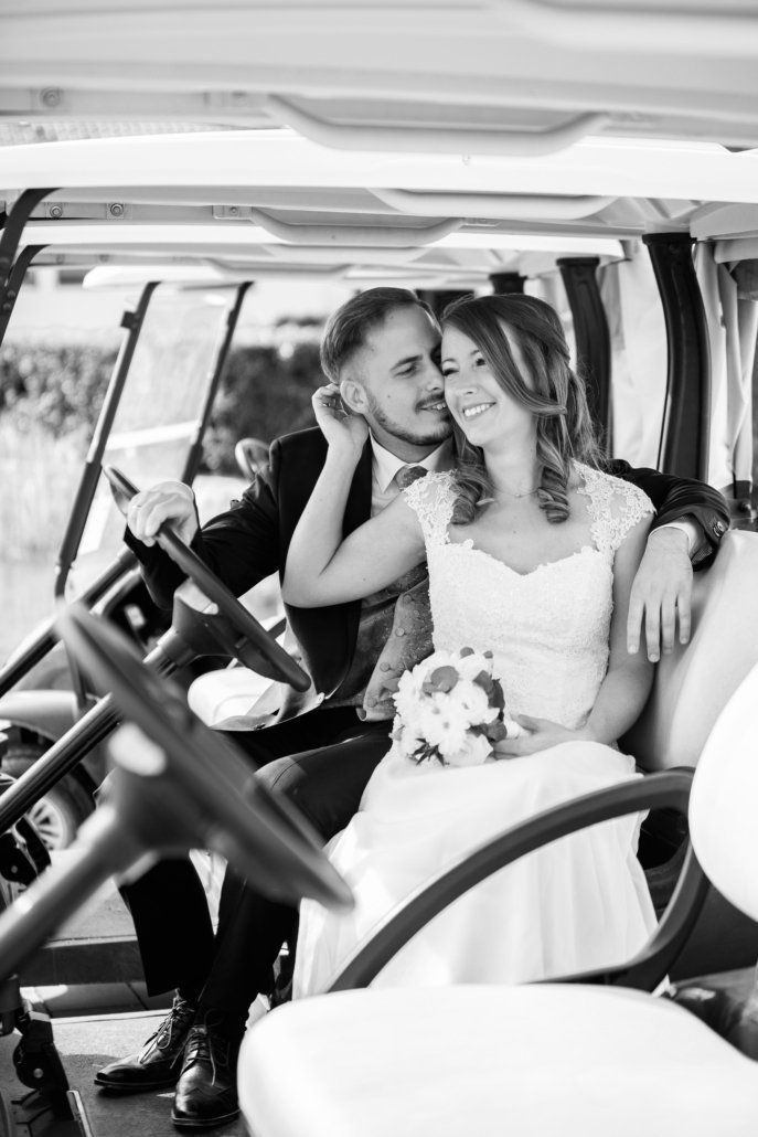 Eine Braut und ein Bräutigam sitzen auf der Rückbank eines Golfwagens.
