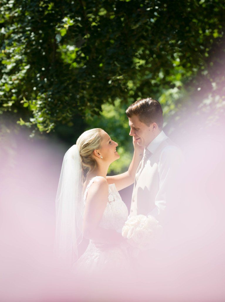 Eine Braut und ein Bräutigam stehen unter einem Baum und schauen einander an.