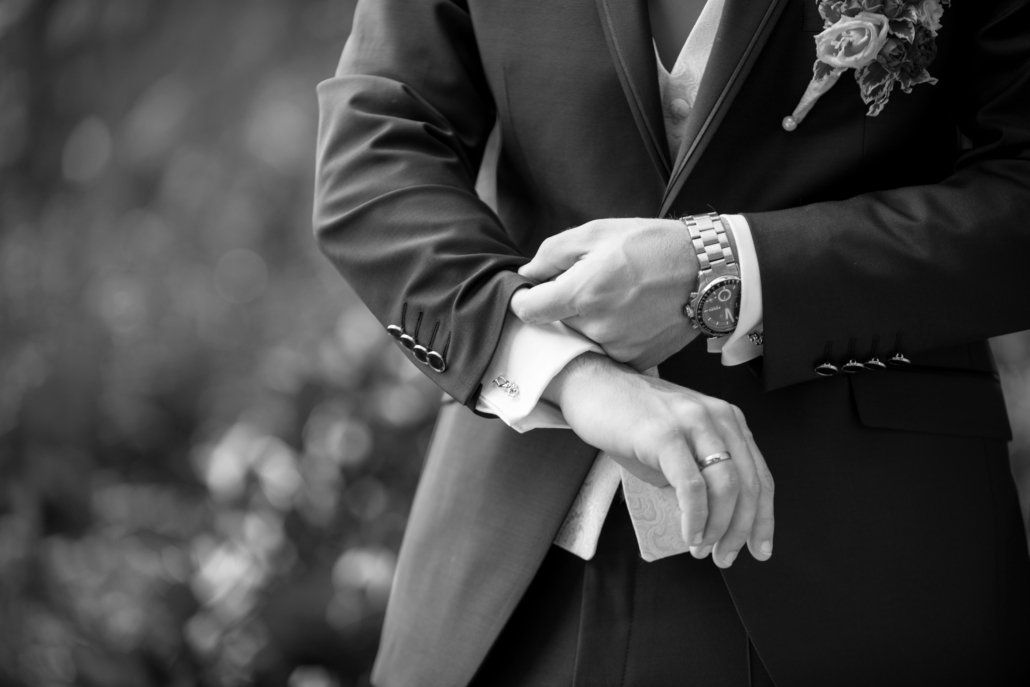 Auf einem Schwarzweißfoto rückt ein Mann im Anzug seine Manschettenknöpfe zurecht.