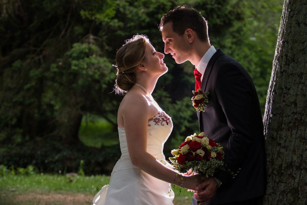 Eine Braut und ein Bräutigam lehnen an einem Baum und küssen sich.