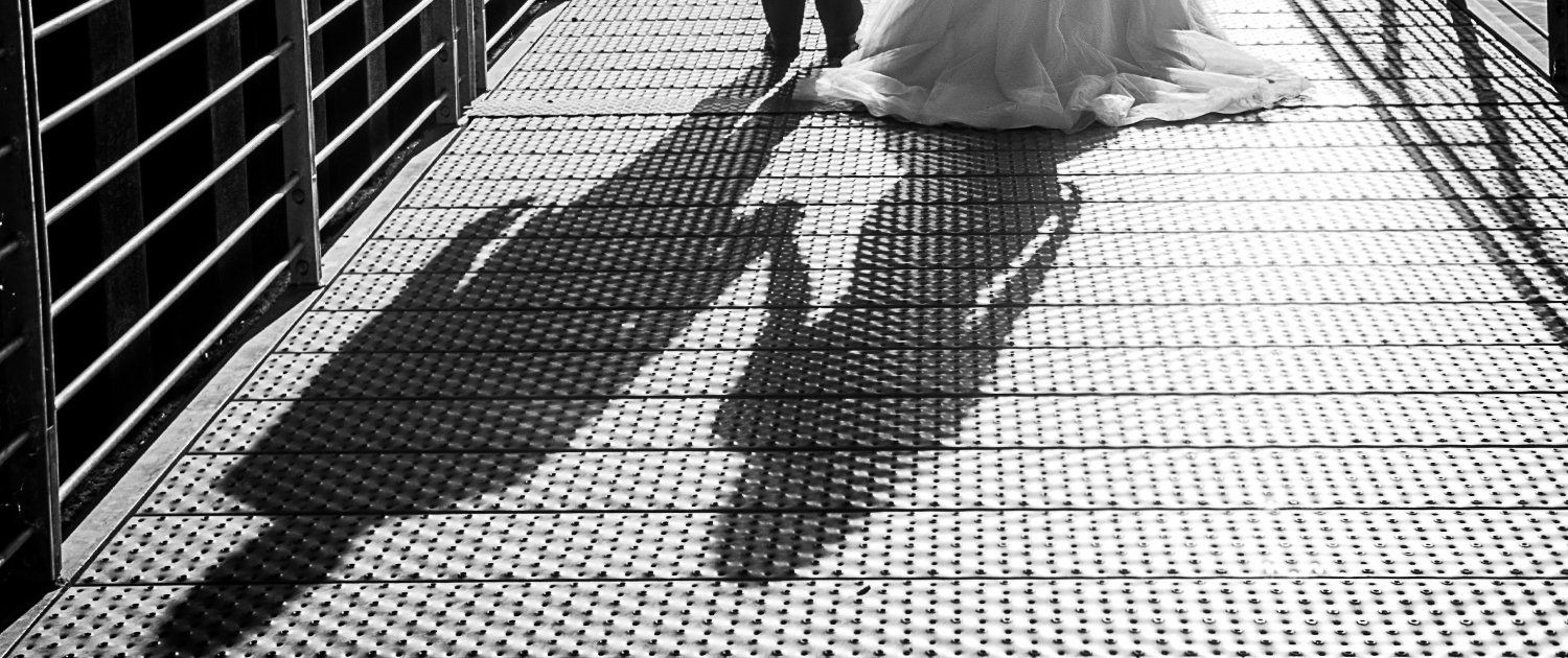 Ein Schwarzweißfoto einer Braut und eines Bräutigams, die über eine Brücke gehen.