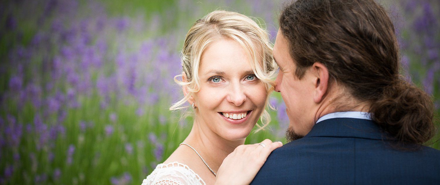 Eine Braut und ein Bräutigam posieren für ein Foto in einem Feld voller lila Blumen.