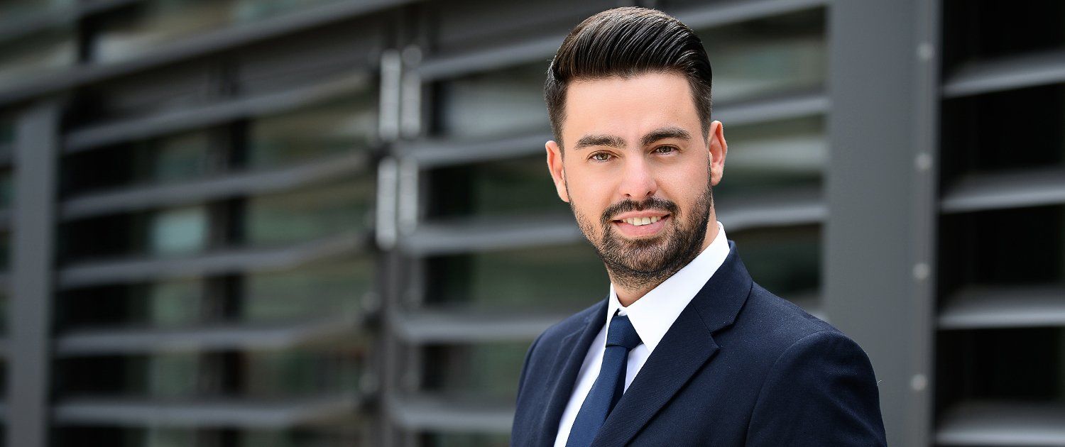 Ein Mann in Anzug und Krawatte steht vor einem Gebäude.